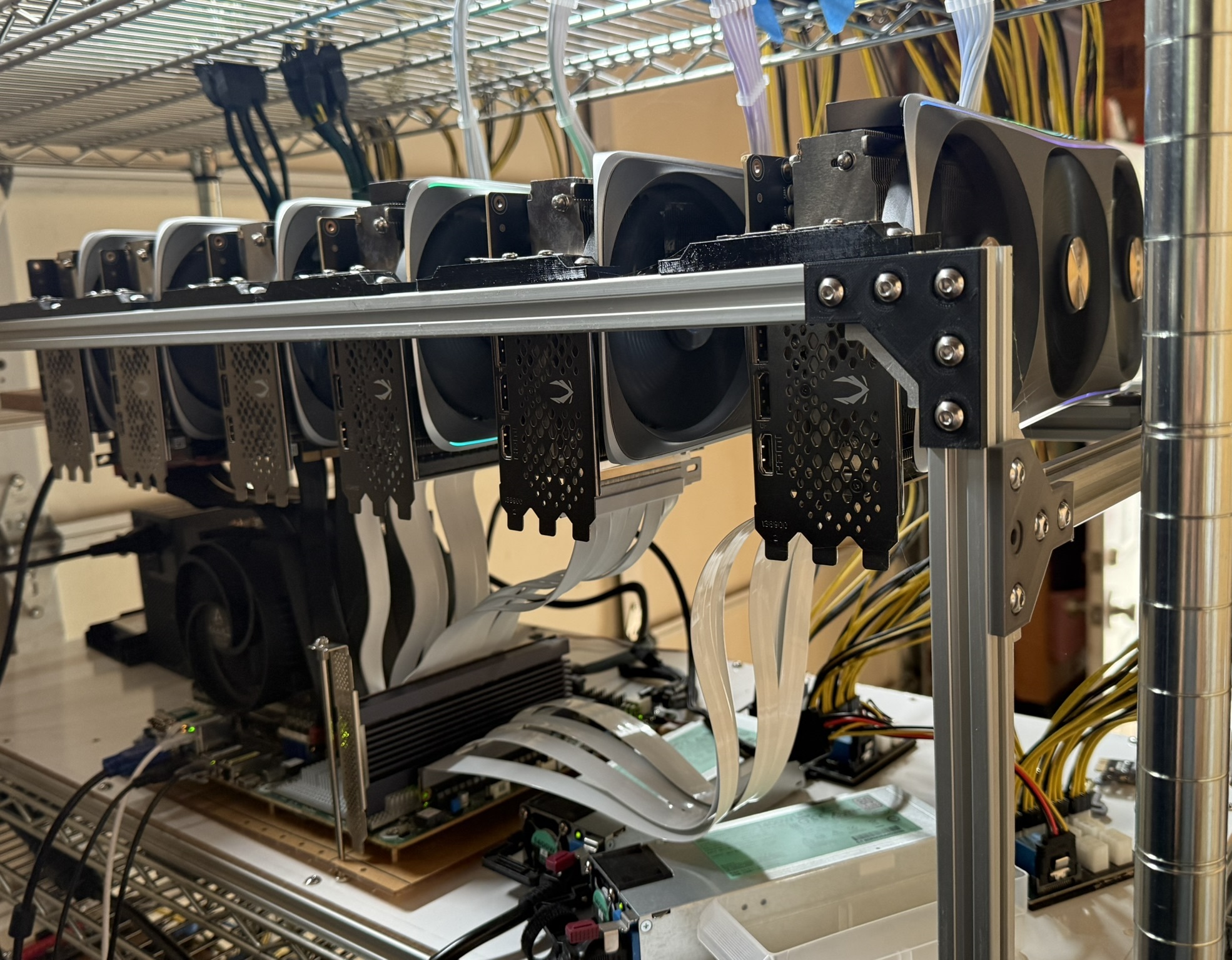 Six NVIDIA GPUs without RGB lighting mounted on an open aluminum-extrusion frame, linked to a motherboard below by white PCIe ribbon extender cables, sitting on a wire shelving unit.