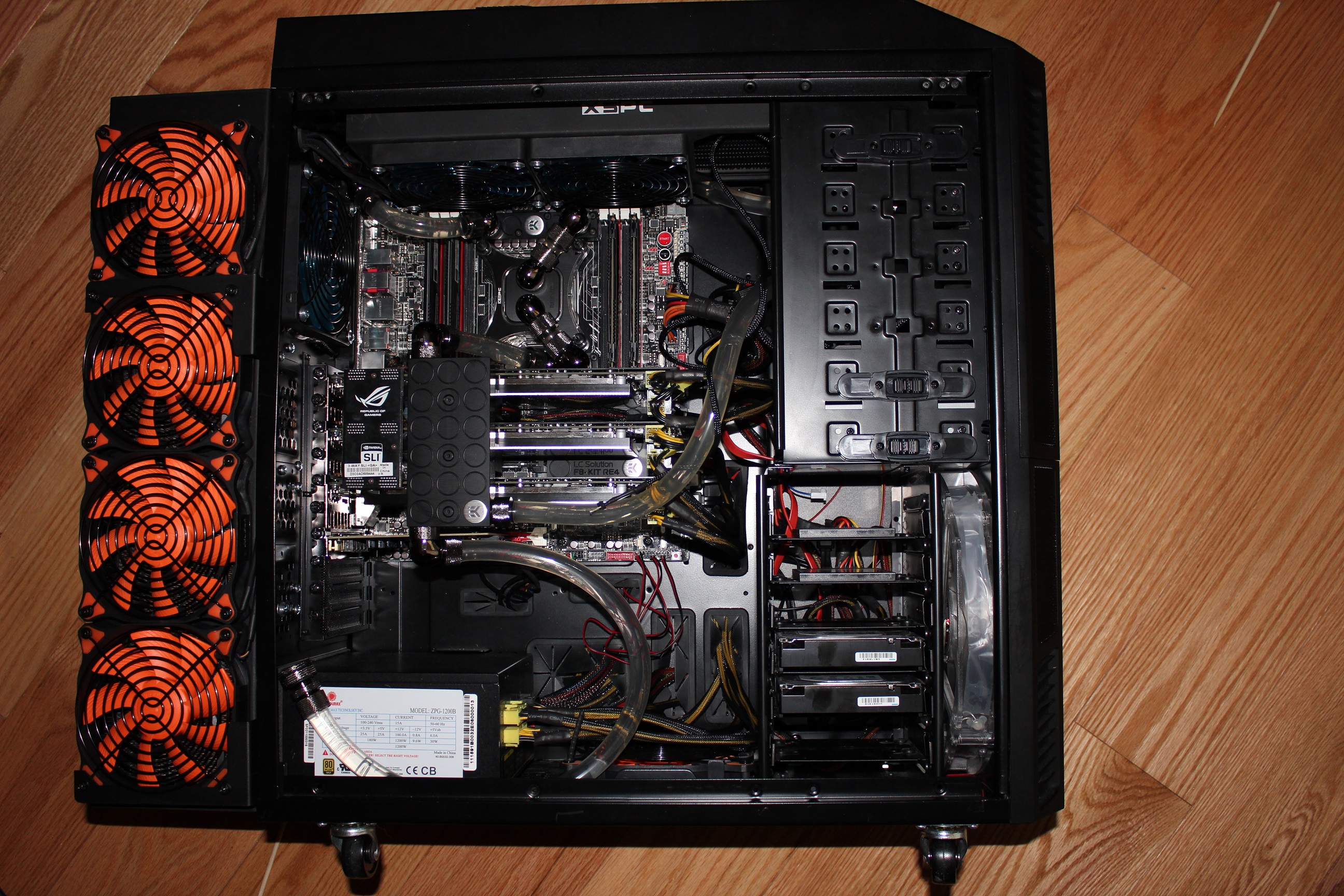 Top-down view inside an open PC case showing a custom water-cooling loop with clear tubing, four orange-bladed intake fans, and an SLI-bridged multi-GPU setup on an ASUS ROG motherboard.